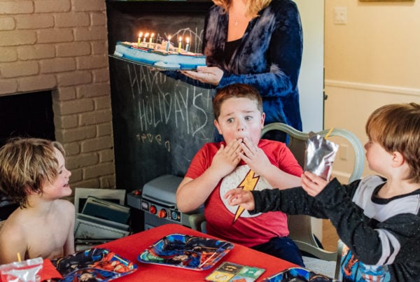 Boy holding his hands to his face as his mom brings him his birthday cake