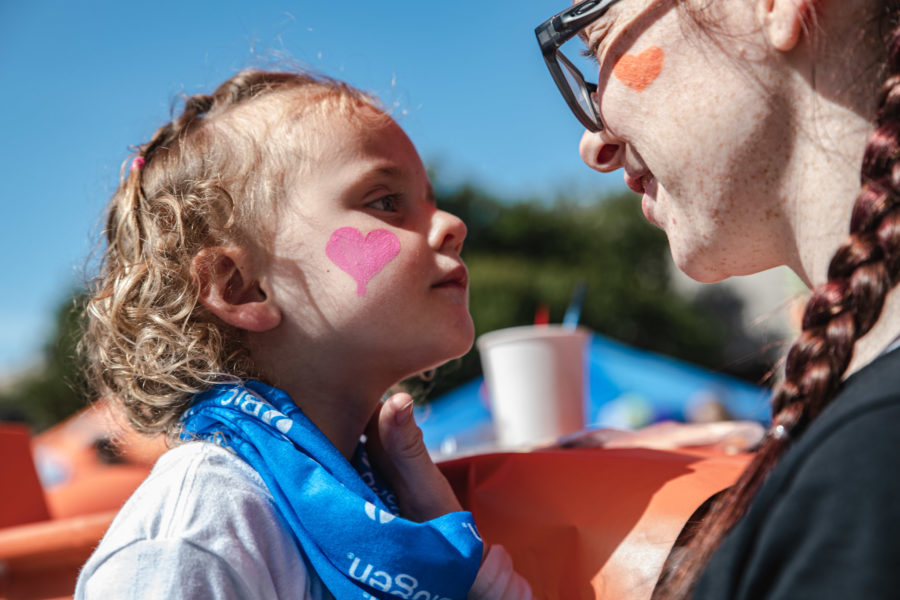 Young girl with pink heart on her cheek stares at older girl with orange heart on her cheek