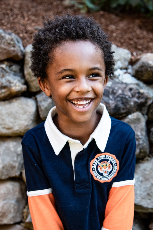A young boy stands in front of a rock wall during school portraits in Oakland, CA