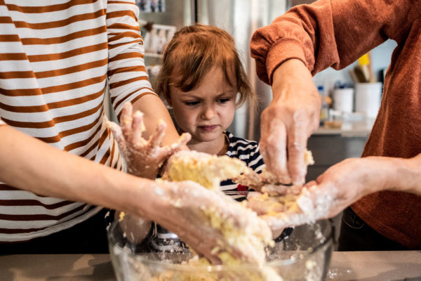A young girl looks at her hands while baking with her mom and grandma in Berkeley, CA