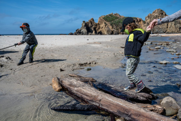 A mom helps her son across a log at Pfeiffer Beach in Big Sur, CA