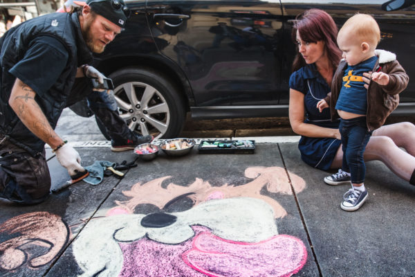 A mom and her son look on as a street artist draws on the sidewalk in San Francisco, CA