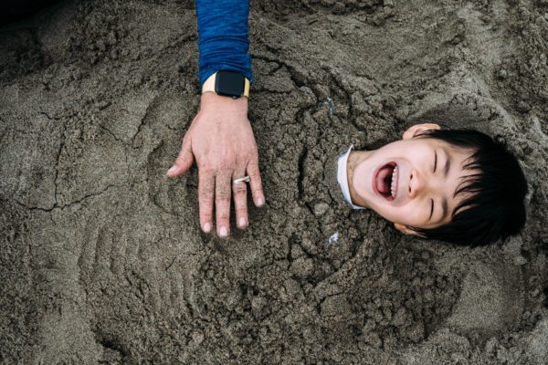 Boy laughs while he is buried in the sand by his mom in Santa Cruz, CA
