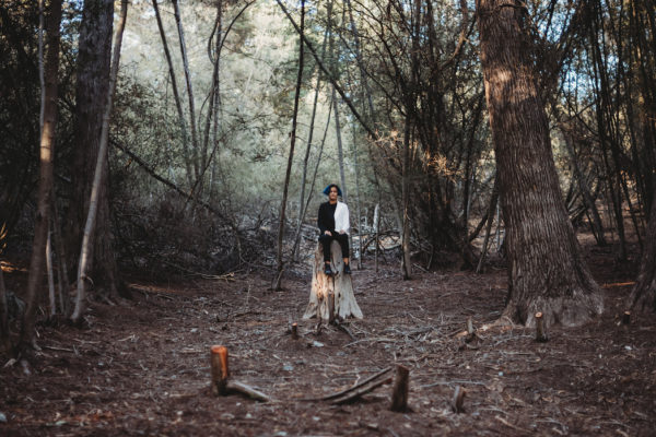 Teen girl sits on a stump in the middle of a forest during a senior photography session in Oakland, CA