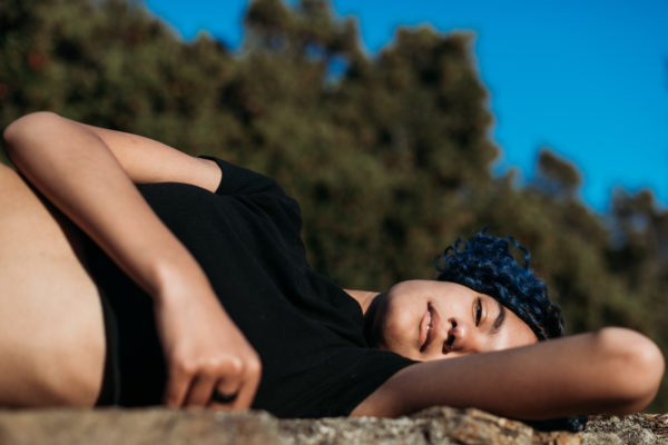 Teen girl lays down on rock wall during a senior photography session in Oakland, CA