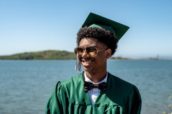 A teen boy poses in cap and gown during a senior photography session in Richmond, CA