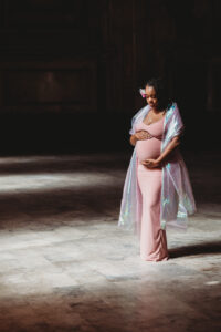 Maternity Photo Shoot with Lisa Winner Photography in Oakland, CA. Women stands in pink dress looking down at her pregnant belly during her maternity photo shoot.