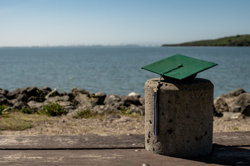 A graduation cap sits on a stump overlooking the San Francisco Bay during a senior photoshoot