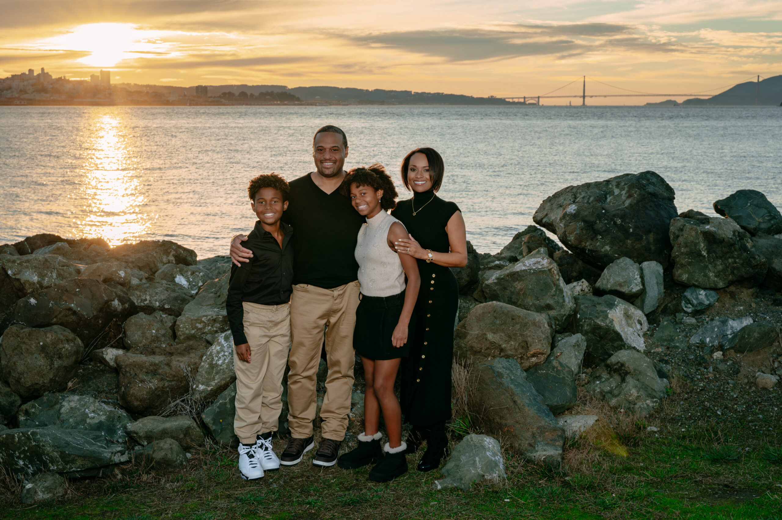 Family of five standing together near San Francisco Bay with Alcatraz and the Golden Gate Bridge in the distance, dressed in neutral tones